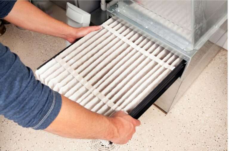 man installing a large air filter in the furnace